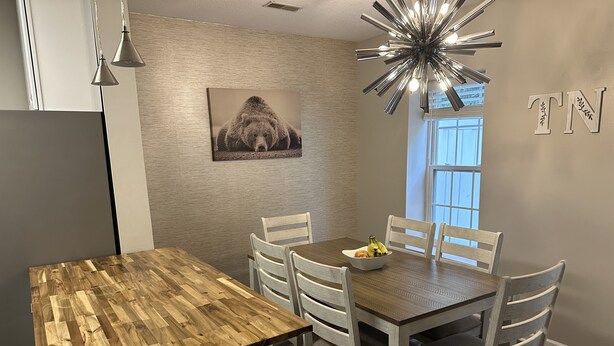 Ein Essbereich mit einem Holztisch, weißen Stühlen, einer Obstschale und einem Bärenbild an der Wand.