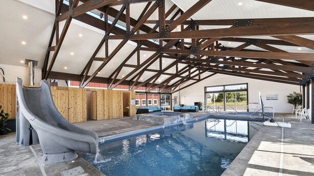 Une piscine intérieure avec un toboggan, des bancs en bois et une vue sur l’extérieur.