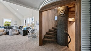 Un salon moderne doté d’un grand canapé d’angle, d’un fauteuil suspendu et d’un escalier avec des éléments en bois.