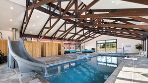 An indoor swimming pool with a slide, wooden deck, and lounge area. - Cedar Farmhouse and Silo w/POOL (Sleeps 50) (Garden City)