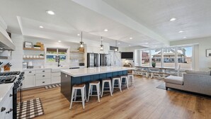A modern kitchen with a central island, bar stools, and a dining area with a view. - Cedar Farmhouse and Silo w/POOL (Sleeps 50) (Garden City)
