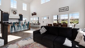 A spacious living area with a black sofa, a patterned rug, and a kitchen area with bar stools. - Cedar Farmhouse and Silo w/POOL (Sleeps 50) (Garden City)