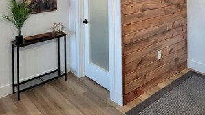 Ein moderner Flur mit einer Wandpaneele aus Holz, einem runden Spiegel, einem Bilderrahmen mit einem abstrakten Gemälde und einer Konsole mit einer Pflanze.