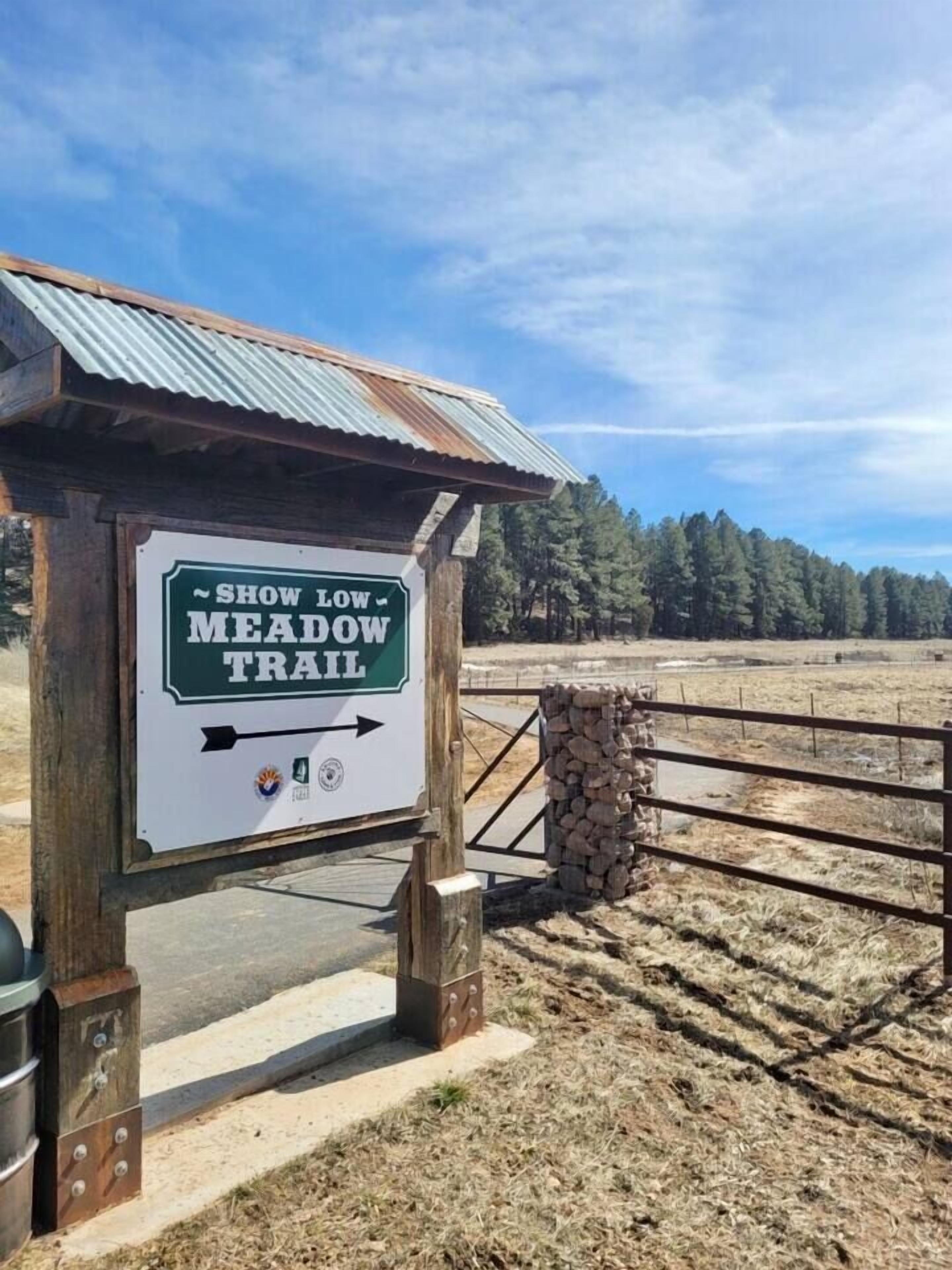 Un segnale di legno rustico per il sentiero Show Low Meadow, con frecce direzionali e loghi.