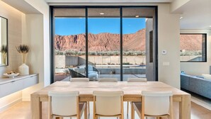 Eine moderne Küche mit großem Esstisch und Stühlen, Blick auf eine Wüstenlandschaft durch große Fenster, und ein minimalistisches Design in neutralen Farben.