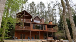 A two-story log cabin with a balcony, surrounded by tall trees.