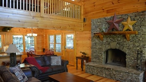 A log cabin interior with a stone fireplace, wooden furniture, and a balcony.
