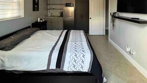 A modern bedroom with a large bed, a ceiling fan, a TV, and a kitchenette in the background. - Luxurious little home! (Hialeah)