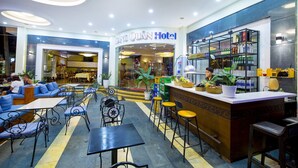 A hotel lobby with seating areas, a bar, and a restaurant visible through the glass doors. - Cocochine a VIE Collection (Da Nang Municipality)