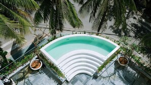 A rooftop pool with a curved design, surrounded by palm trees and potted plants. - Cocochine a VIE Collection (Da Nang Municipality)