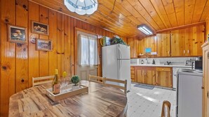 A wooden cabin interior with a dining table, chairs, a refrigerator, and a kitchen area. - Rivers Resort Cabin #2 (Strawberry)