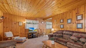 A cozy log cabin interior with a sofa, chairs, a television, and a wooden table. - Rivers Resort Cabin #2 (Strawberry)