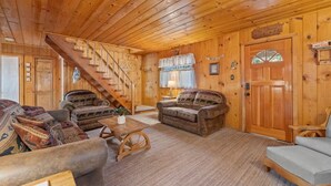 A log cabin interior with a wooden staircase, two sofas with animal prints, a wooden coffee table, and a door with a window. - Rivers Resort Cabin #2 (Strawberry)