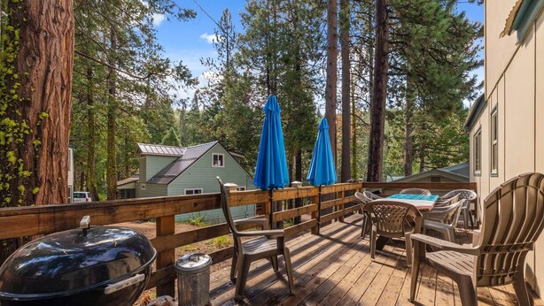A wooden deck with outdoor furniture, a grill, and a trash can. - Rivers Resort Cabin #2 (Strawberry)