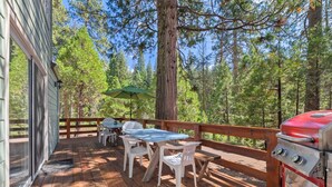 Une terrasse en bois équipée d’un barbecue, d’une table de pique-nique et de chaises, le tout entouré d’arbres.