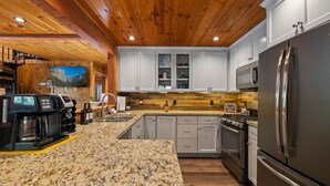 Une cuisine moderne dotée de plans de travail en granit, d’appareils électroménagers en acier inoxydable et de poutres en bois au plafond.