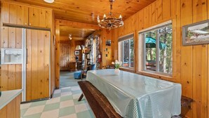 A cabin interior with wooden walls, a checkered table, a bench, and a chandelier.