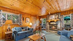 A cozy cabin interior with wooden walls, a stone fireplace, and a blue sofa set.