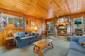 A cozy cabin interior with wooden walls, a stone fireplace, and a blue sofa set. - Rivers Resort Cabin #5 (Strawberry)