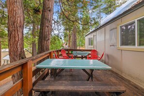 A wooden deck with a picnic table and red chairs, surrounded by large trees. - Rivers Resort Cabin #6 (Strawberry)