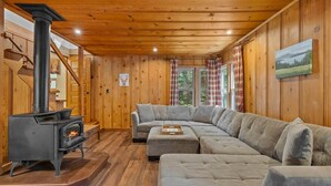 Un acogedor interior de cabaña con estufa de leña, un amplio sofá modular y paredes de madera.