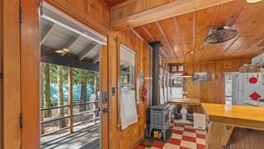 Interior de una cabaña de madera con piso a cuadros, una zona de cocina y vista a una terraza exterior a través de una puerta de cristal.