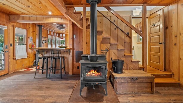 Interior acogedor de una cabaña con estufa de leña, paredes de madera, una zona de bar y una escalera.