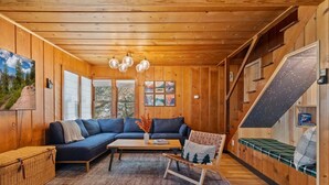 Interior acogedor de una cabaña con detalles de madera, un sofá modular, una mesita, un banco y una escalera.