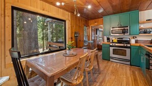 Interior de una cabaña de madera con una mesa de comedor, sillas, una cocina con armarios verdes, una estufa y un microondas.