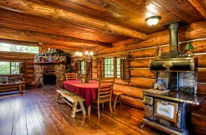 A cozy cabin interior with a stone fireplace, wooden dining table, and a vintage stove.