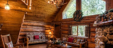 A log cabin interior with a fireplace, wooden furniture, and a chandelier.