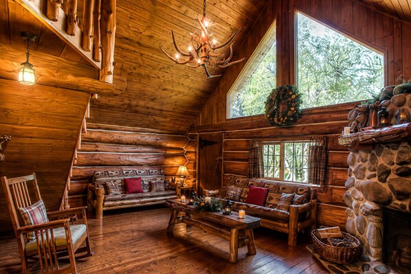 A log cabin interior with a fireplace, wooden furniture, and a chandelier. - Charming, Rustic Log Home on Edge of South Fork River (Raymond)