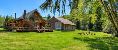 A log cabin with a porch and a separate building, surrounded by a well-maintained lawn and trees.