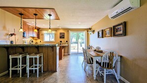Een keuken met houten kastjes, een centraal eiland, barstoelen en een eettafel met stoelen.