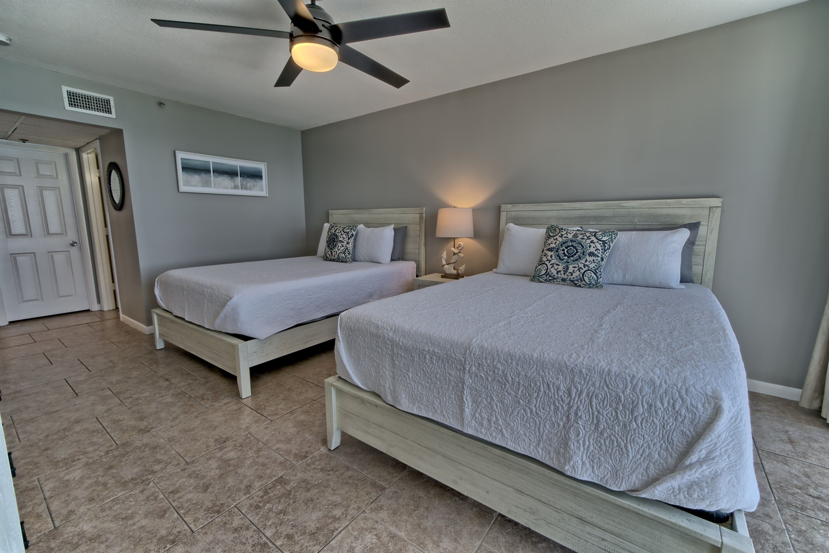 A bedroom with two beds, a ceiling fan, a window, and a door.
