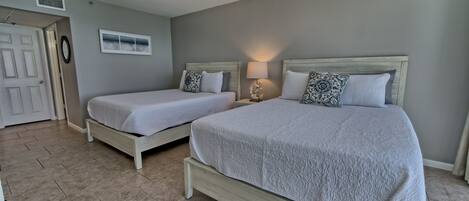 A bedroom with two beds, a ceiling fan, a window, and a door.