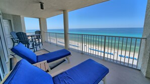 A balcony with two blue lounge chairs, a small table, and a view of the beach and ocean.