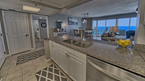 A modern kitchen with granite countertops, a double sink, and a dining area with a view of the ocean.