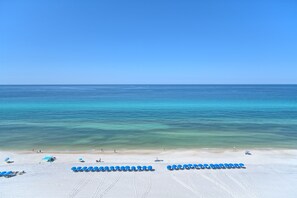 Une plage bordée de rangées de chaises longues bleues et d’un rivage sablonneux.