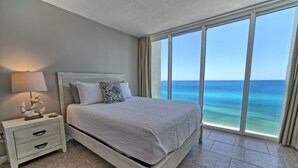 A bedroom with a bed, a nightstand, and a view of the ocean.