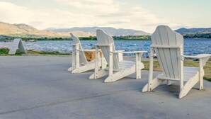 Trois chaises Adirondack sont disposées face à un plan d’eau, avec des montagnes en arrière-plan.
