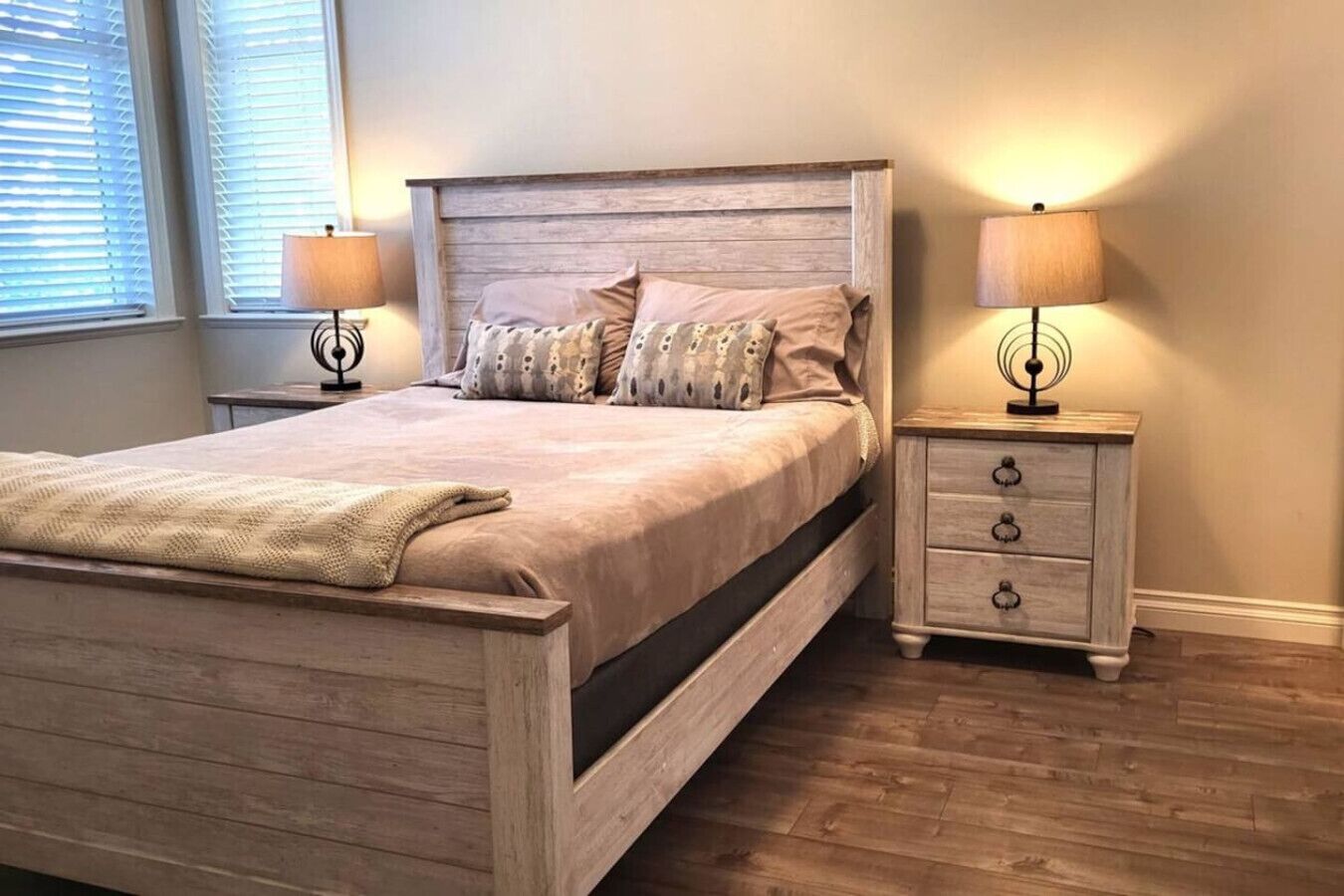 Une chambre à coucher avec un lit en bois, deux tables de chevet avec des lampes, une commode et une fenêtre avec des stores.