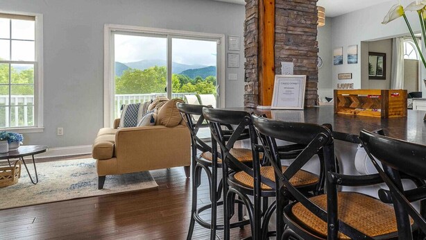 Sala de estar com sofá, cadeiras, mesa de jantar e vista para montanhas por grandes janelas.