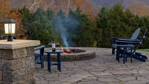 Uma área externa com espaço para sentar, lareira, mesa de pedra e cadeiras Adirondack.