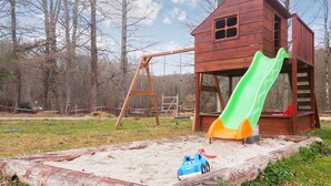 Une cabane en bois avec un toboggan et une balançoire, située dans un espace boisé.