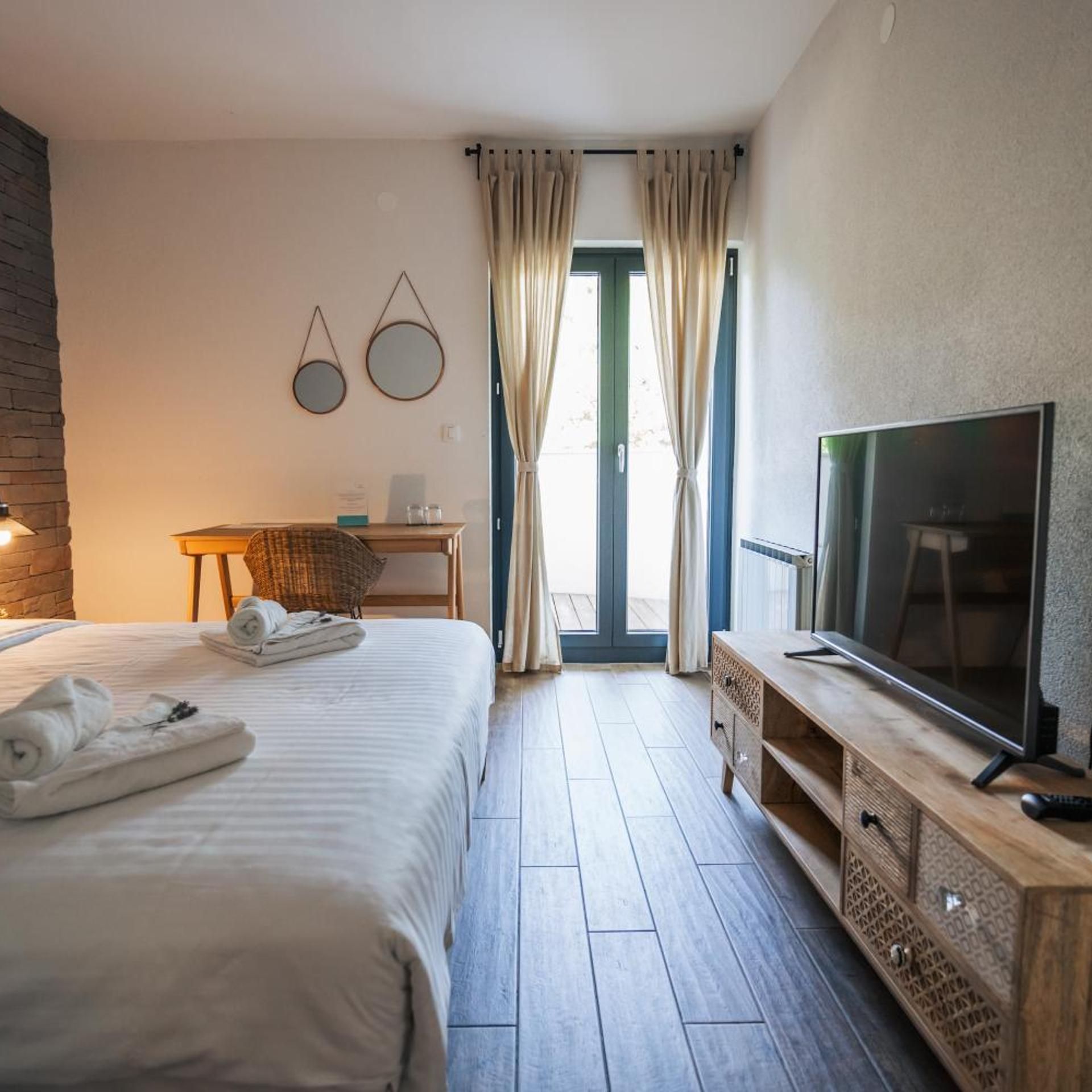 Ein Hotelzimmer mit Bett, Fernseher, Schreibtisch und Blick durch eine Glastür.