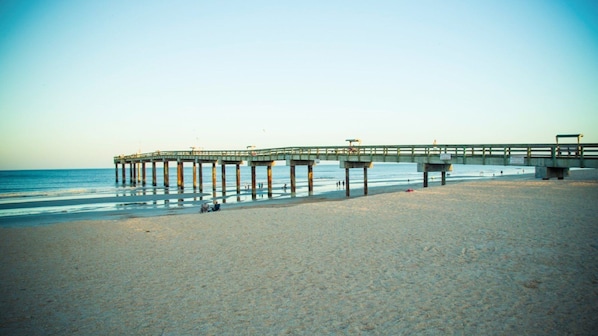 Un muelle que se adentra en el mar, con una playa arenosa al frente.