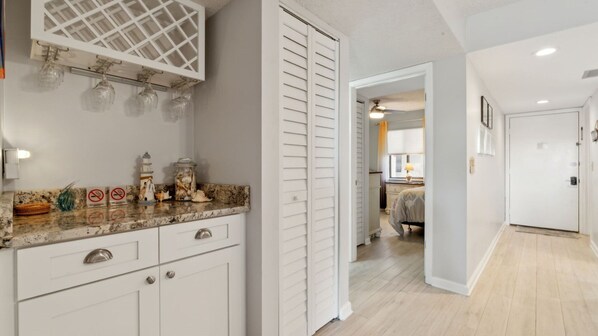 A kitchen with white cabinets, a marble countertop, and a glass wine rack.