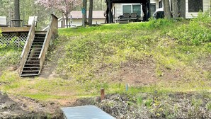Un quartier résidentiel avec un escalier en bois menant à une terrasse, un espace extérieur couvert aménagé en coin salon et une maison dont on peut voir une fenêtre.