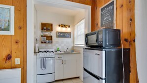 Une cuisine compacte avec des meubles blancs, un réfrigérateur en acier inoxydable, un four à micro-ondes et une cuisinière à gaz. Un tableau noir est accroché au mur et une image encadrée se trouve au-dessus de l’évier.
